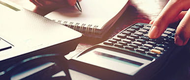 Close up woman hand using calculator and writing make note with calculate about cost at home office.